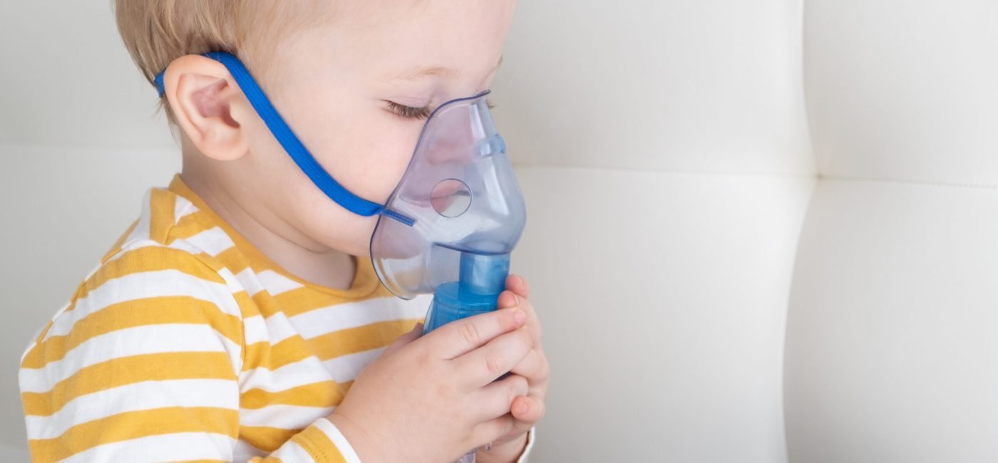 Little baby boy himself using steam inhaler nebulizer mask himself on the bed. copy space