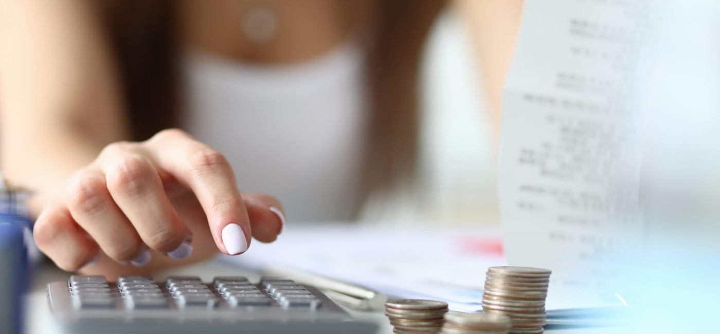 Focus on tender hands of witty businesswoman sitting indoors and using calculator for counting in important tablet with charts. Office concept. Blurred background